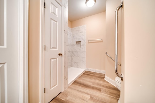 bathroom featuring a tile shower, wood finished floors, toilet, and baseboards
