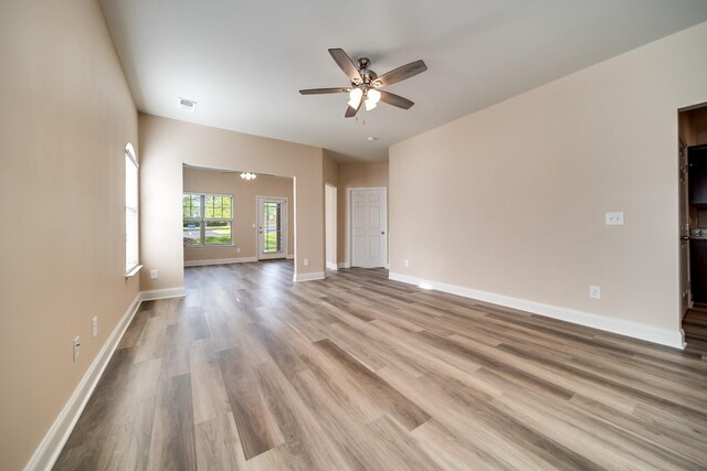 unfurnished living room with wood finished floors, visible vents, baseboards, and ceiling fan