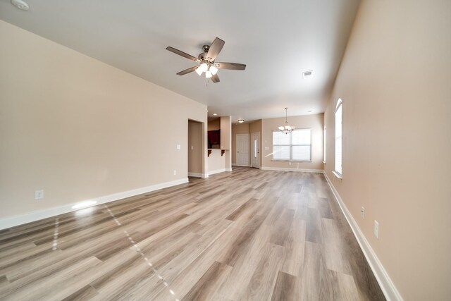 unfurnished living room with light wood-style floors, visible vents, baseboards, and ceiling fan with notable chandelier