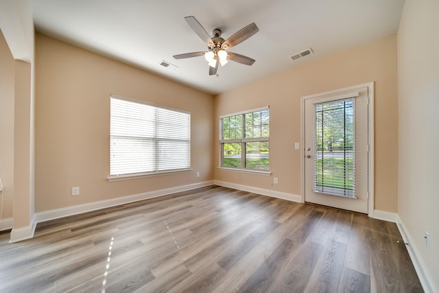 unfurnished room with wood finished floors, visible vents, a ceiling fan, and baseboards