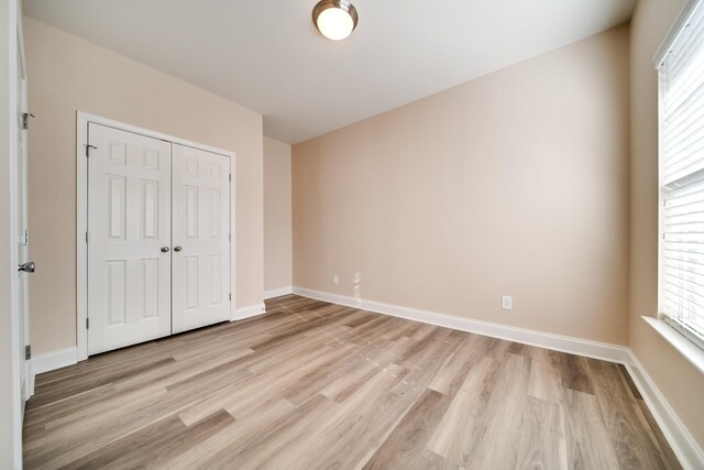 unfurnished bedroom featuring light wood finished floors, a closet, and multiple windows