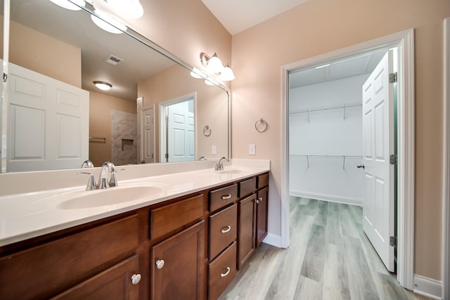 full bath with a sink, double vanity, visible vents, a spacious closet, and wood finished floors