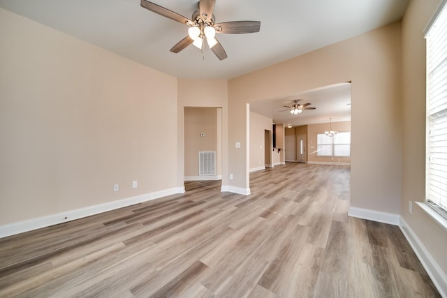 spare room with ceiling fan with notable chandelier, baseboards, light wood-style flooring, and visible vents