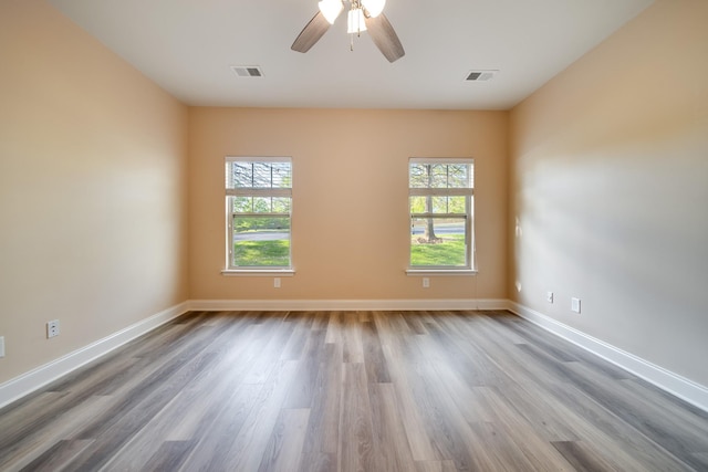 empty room with wood finished floors, visible vents, ceiling fan, and a healthy amount of sunlight