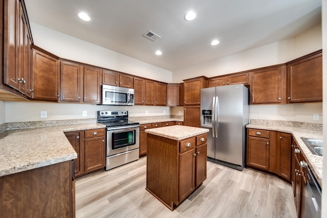 kitchen with stainless steel appliances, a sink, light wood-type flooring, visible vents, and a kitchen island