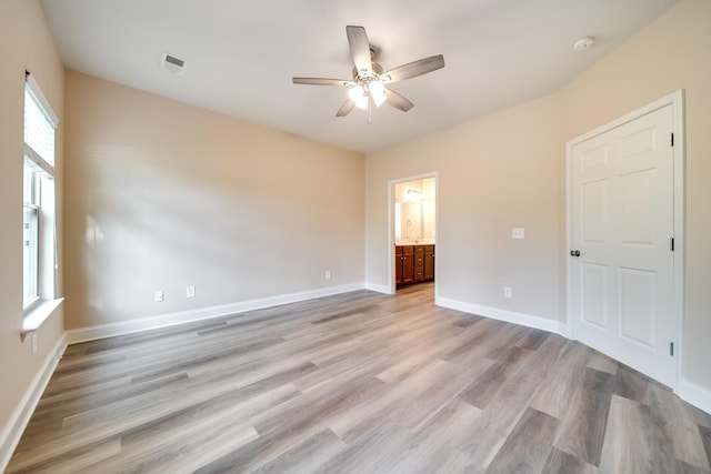 unfurnished bedroom featuring light wood-style flooring, baseboards, visible vents, a ceiling fan, and ensuite bath