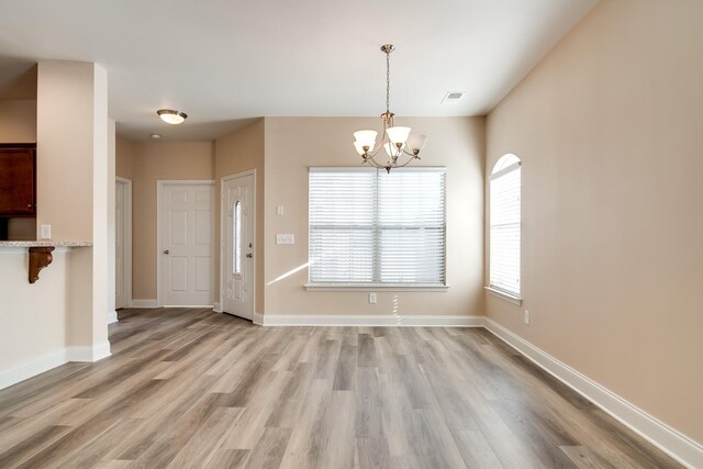 unfurnished dining area featuring light wood-style floors, visible vents, baseboards, and an inviting chandelier