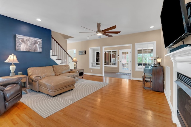 living room featuring light wood-style floors, recessed lighting, a fireplace, a ceiling fan, and stairs