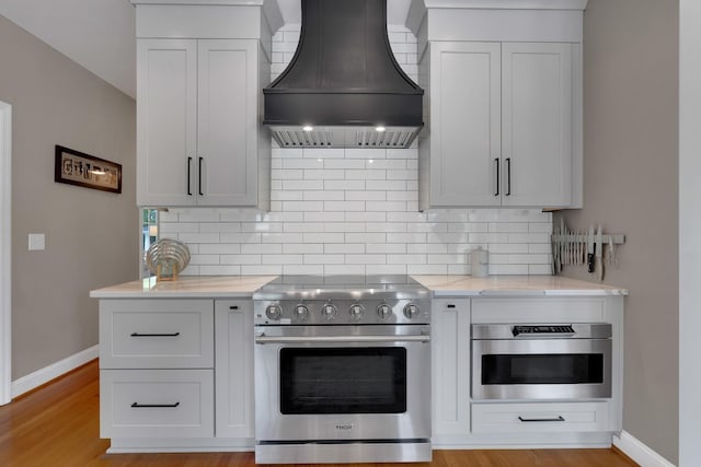 kitchen with baseboards, decorative backsplash, high end range, light wood-type flooring, and premium range hood
