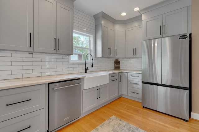 kitchen with light stone countertops, a sink, decorative backsplash, light wood-style floors, and appliances with stainless steel finishes