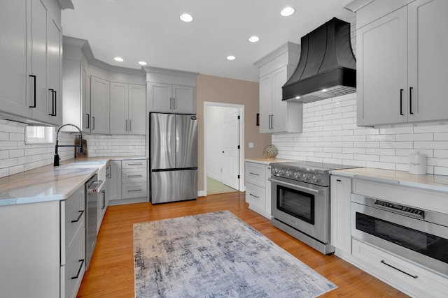kitchen featuring tasteful backsplash, light stone counters, stainless steel appliances, custom range hood, and a sink