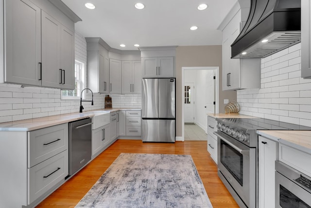 kitchen featuring light stone counters, decorative backsplash, custom range hood, a sink, and stainless steel appliances