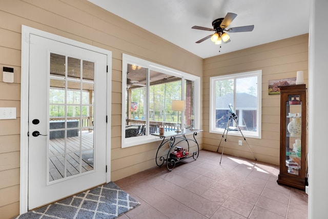 doorway to outside with wooden walls, ceiling fan, and tile patterned floors