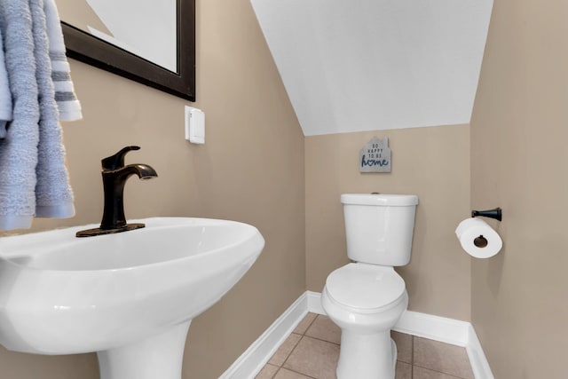half bathroom featuring tile patterned floors, vaulted ceiling, toilet, a sink, and baseboards