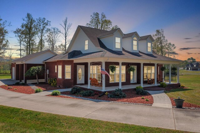 view of front of house featuring a porch, a lawn, driveway, and brick siding
