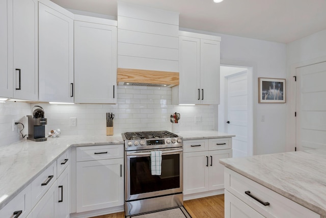 kitchen with stainless steel gas range, decorative backsplash, and white cabinetry