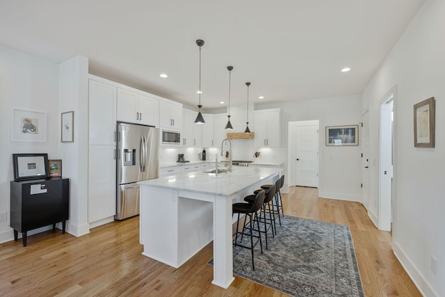 kitchen featuring appliances with stainless steel finishes, light wood finished floors, white cabinetry, a breakfast bar area, and an island with sink
