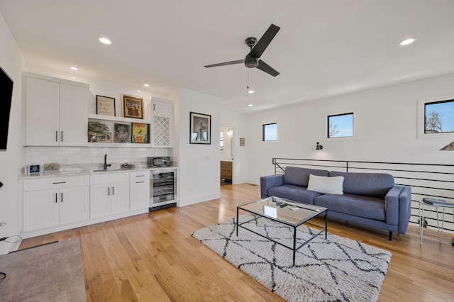 living room with beverage cooler, bar with sink, ceiling fan, light wood-style flooring, and recessed lighting