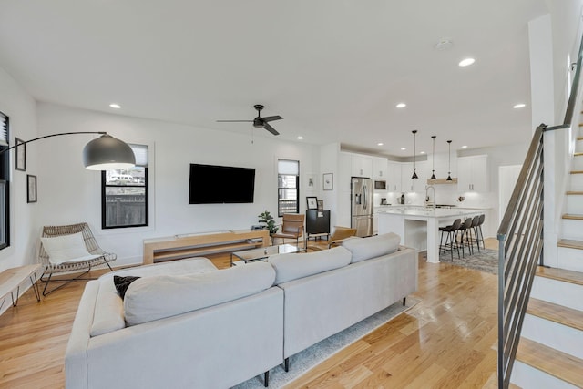living area featuring stairway, a ceiling fan, light wood-type flooring, and recessed lighting