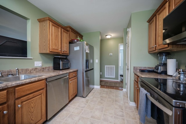 kitchen with visible vents, a sink, baseboards, brown cabinetry, and appliances with stainless steel finishes