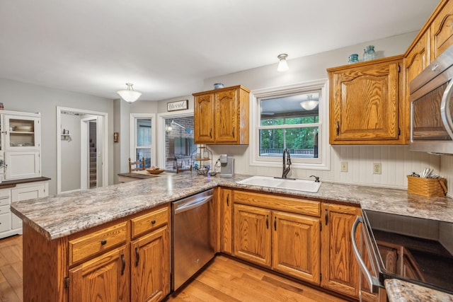 kitchen with a sink, brown cabinets, light wood-style floors, a peninsula, and appliances with stainless steel finishes