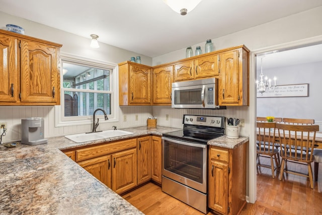 kitchen with light wood-style flooring, a sink, a notable chandelier, brown cabinets, and appliances with stainless steel finishes