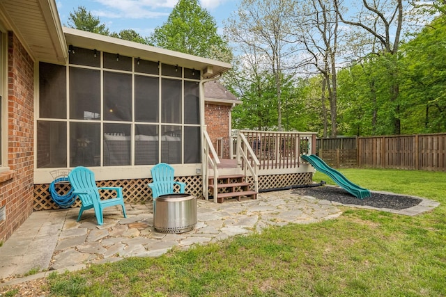 view of patio / terrace featuring a wooden deck, a sunroom, a fenced backyard, and a playground