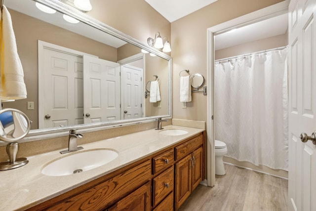bathroom featuring double vanity, wood finished floors, toilet, and a sink