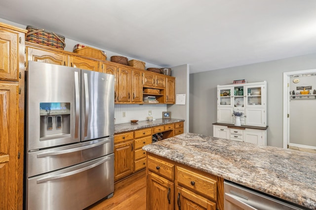 kitchen featuring light wood-type flooring, light stone counters, stainless steel fridge with ice dispenser, open shelves, and brown cabinetry