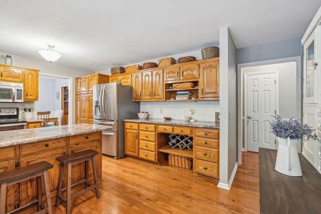 kitchen with a kitchen breakfast bar, open shelves, brown cabinetry, light wood-style flooring, and appliances with stainless steel finishes