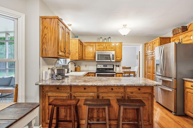 kitchen featuring a peninsula, a sink, light wood-style floors, light countertops, and appliances with stainless steel finishes