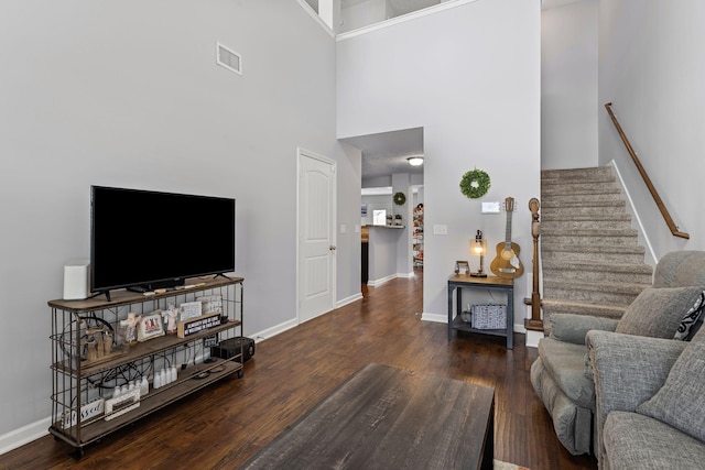 living room featuring baseboards, visible vents, a towering ceiling, wood finished floors, and stairway