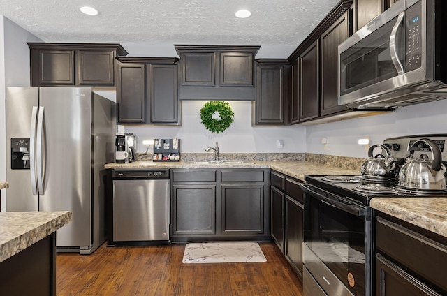 kitchen with stainless steel appliances, light countertops, a sink, dark wood-type flooring, and a textured ceiling