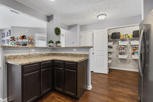 kitchen with dark wood finished floors, a textured ceiling, visible vents, and freestanding refrigerator