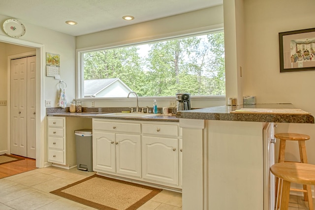 kitchen featuring tile counters, white cabinetry, light tile patterned floors, a sink, and a breakfast bar area