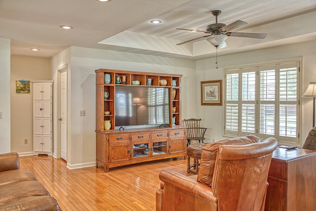 living area with a ceiling fan, light wood-type flooring, a raised ceiling, baseboards, and recessed lighting