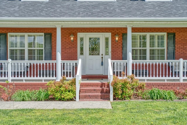 entrance to property featuring brick siding, a shingled roof, and covered porch