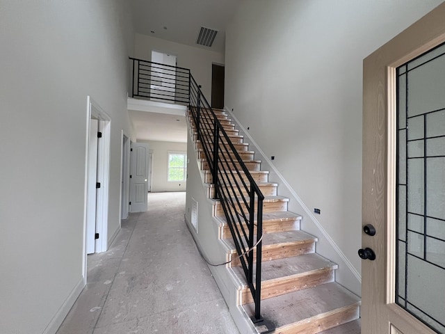 staircase with baseboards, visible vents, a high ceiling, and unfinished concrete floors