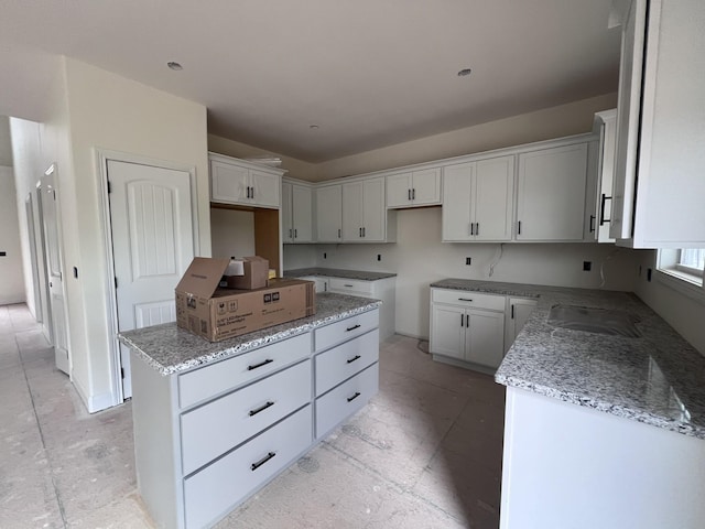 kitchen featuring a center island, a sink, white cabinetry, and light stone counters