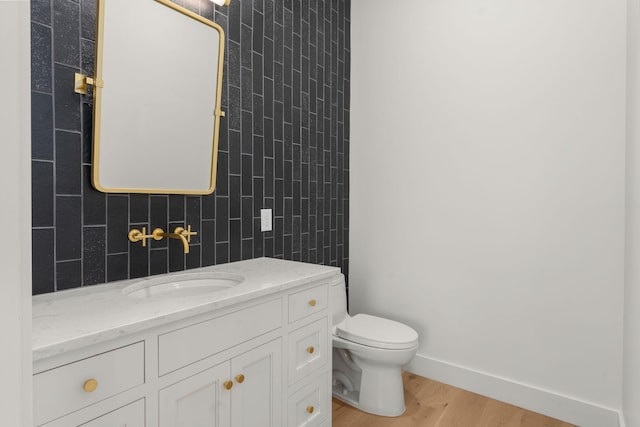 half bath with toilet, vanity, tile walls, and wood finished floors