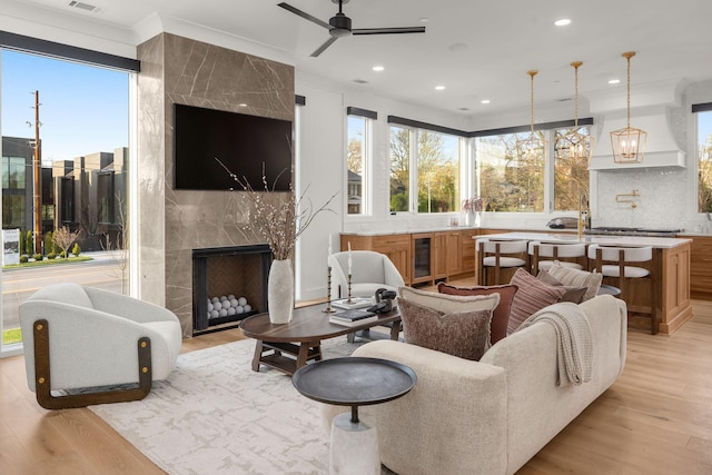 living room with wine cooler, ceiling fan, a high end fireplace, and light wood-style floors