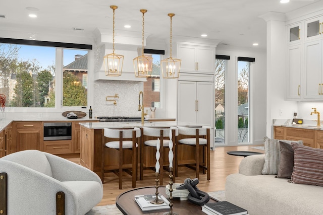 kitchen with stainless steel microwave, light wood-style flooring, glass insert cabinets, an inviting chandelier, and recessed lighting