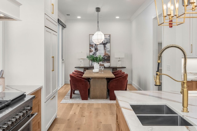 kitchen with light wood finished floors, light stone countertops, an inviting chandelier, a sink, and hanging light fixtures