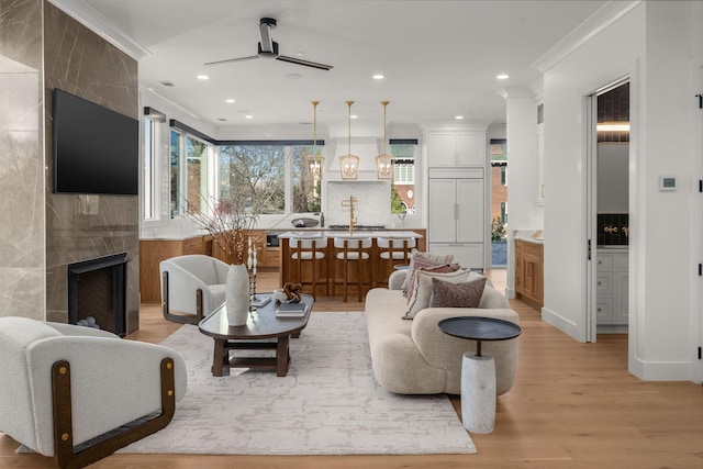 living area with light wood finished floors, recessed lighting, a fireplace, crown molding, and a ceiling fan