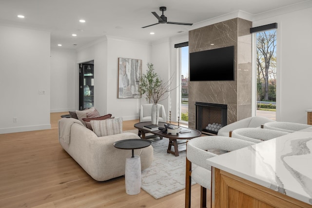 living room with a high end fireplace, ornamental molding, ceiling fan, and light wood-style floors
