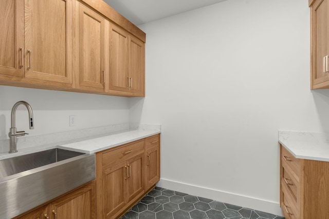 kitchen with baseboards, dark tile patterned flooring, and a sink