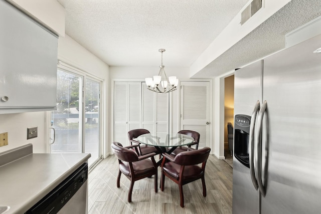 dining area featuring a textured ceiling, light wood-type flooring, a chandelier, and visible vents