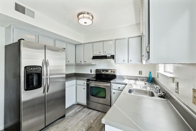 kitchen with a sink, light wood-style flooring, stainless steel appliances, under cabinet range hood, and visible vents