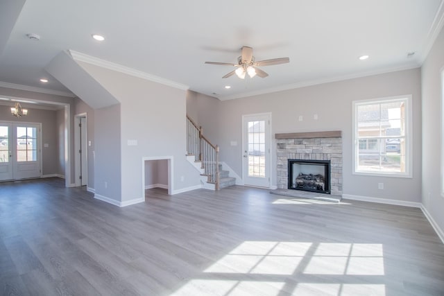 unfurnished living room with a stone fireplace, wood finished floors, a wealth of natural light, and stairway