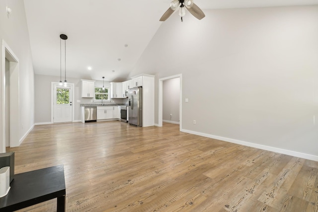 unfurnished living room featuring light wood-style floors, ceiling fan, a sink, baseboards, and high vaulted ceiling